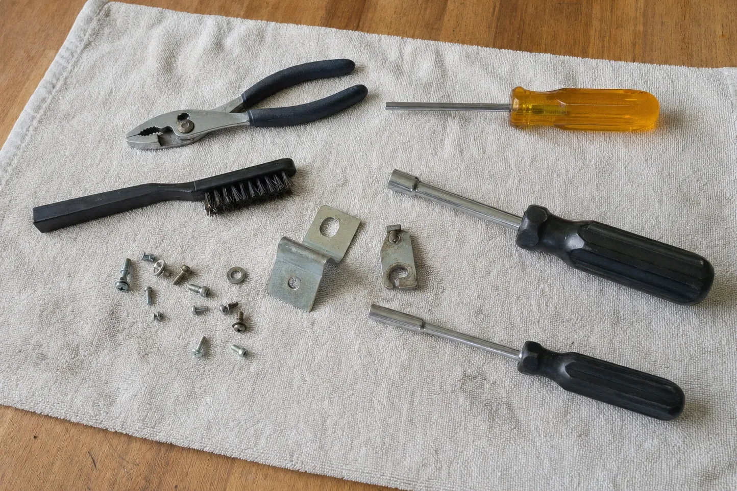 Slip-joint pliers, a pry bar, a wire brush, a screwdriver and two nut drivers on a towel with loose screws