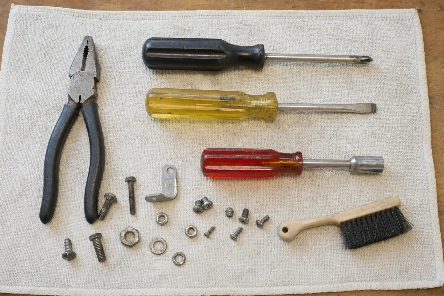 Combination pliers, a Phillips driver, a flat driver, a nut driver and a cream-handled brush around a small angle bracket and loose fixings
