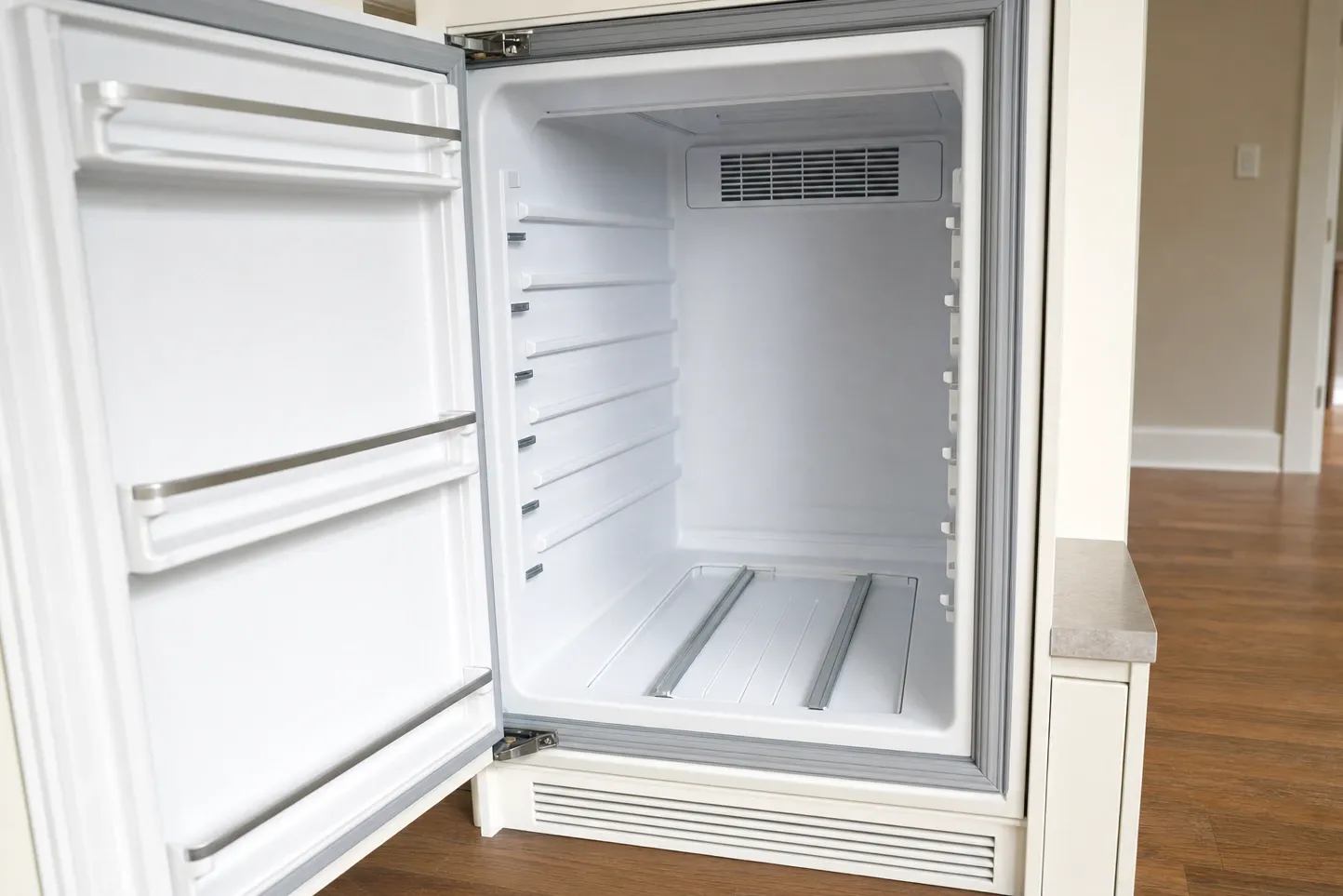 Built-in undercounter refrigerator standing open on a bare white liner, the door gasket running right round the opening